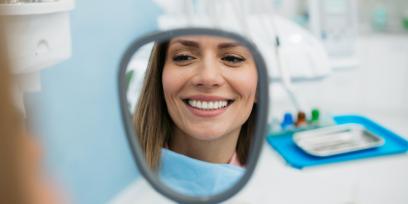 Patientin lächelt zufrieden mit Blick in einen Handspiegel