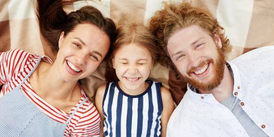 Familie liegt lächelnd gemeinsam auf einer Decke